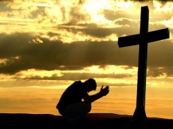 Uomo prega inginocchiato dinanzi ad una croce
